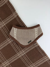 A close-up of a brown and cream plaid knit garment, showing a folded collar or neck area with striped and cable-knit detailing on a plain light background.