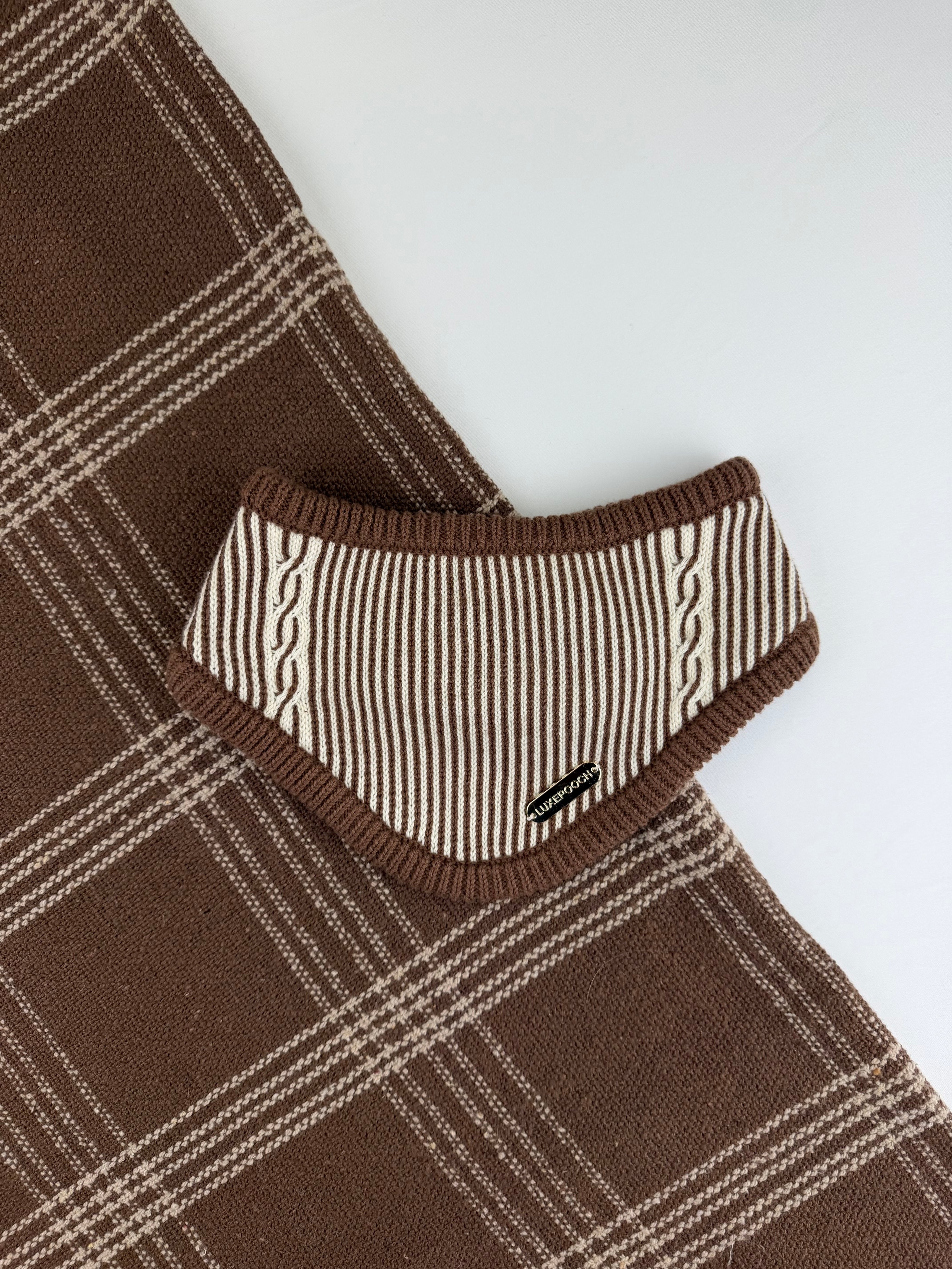 A close-up of a brown and cream plaid knit garment, showing a folded collar or neck area with striped and cable-knit detailing on a plain light background.