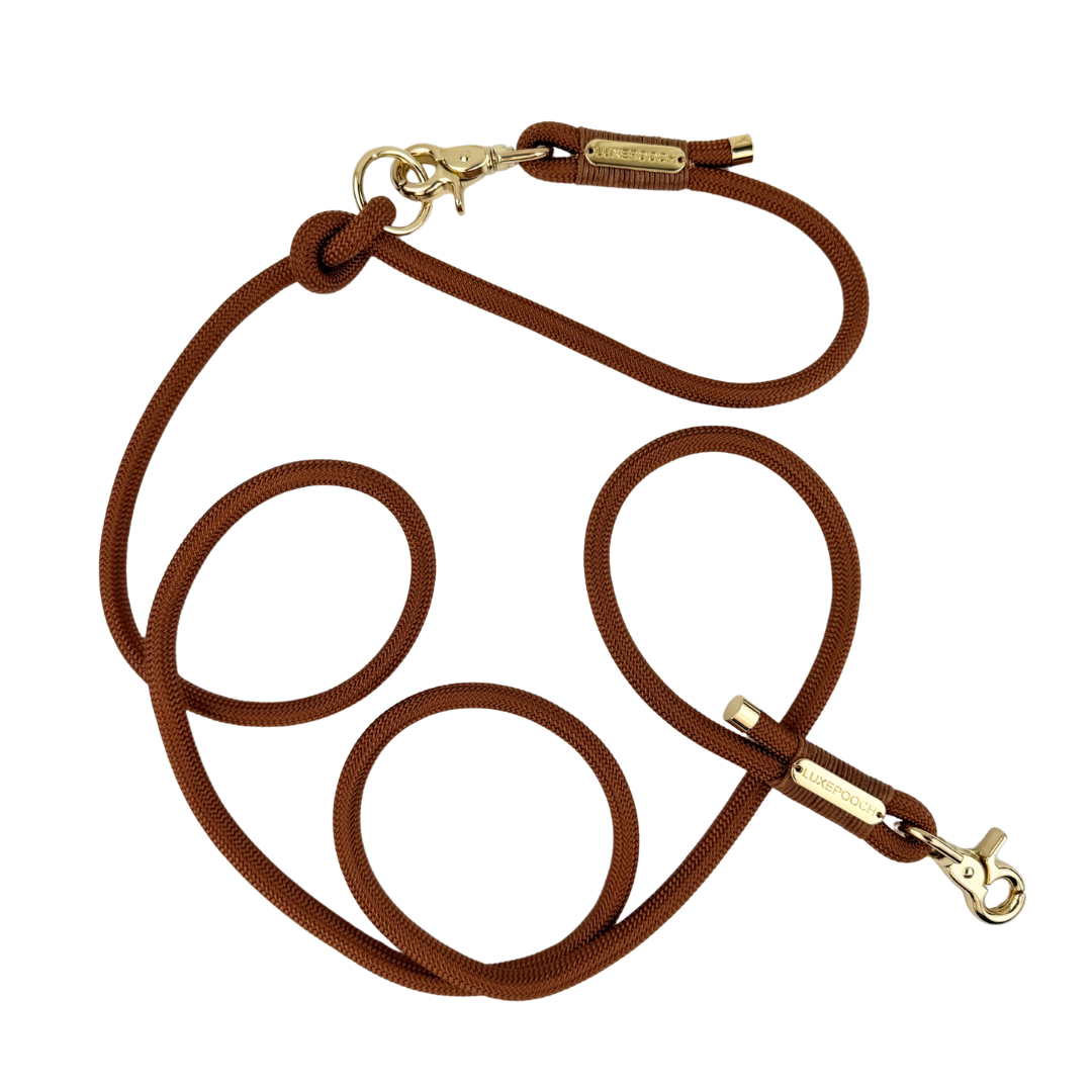 A brown rope dog leash with gold-tone metal hardware, including a snap hook clasp and a small brand tag, displayed on a clean white background.